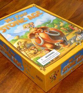 Board game box for "My First Stone Age," featuring colorful illustrations of early humans and a woolly mammoth, designed for ages 2-4, suitable for 2-4 players, with a playtime of 15 minutes.