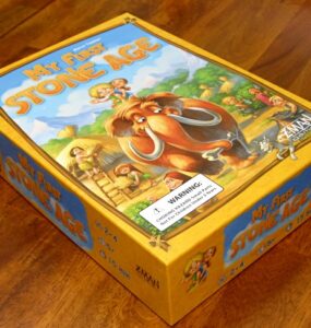 Board game box for "My First Stone Age," featuring colorful illustrations of early humans and a woolly mammoth, designed for ages 2-4, suitable for 2-4 players, with a playtime of 15 minutes.