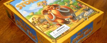 Board game box for "My First Stone Age," featuring colorful illustrations of early humans and a woolly mammoth, designed for ages 2-4, suitable for 2-4 players, with a playtime of 15 minutes.