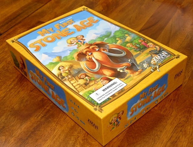 Board game box for "My First Stone Age," featuring colorful illustrations of early humans and a woolly mammoth, designed for ages 2-4, suitable for 2-4 players, with a playtime of 15 minutes.