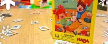 Colorful board game "Tidy Toyboxes" by HABA, featuring playful illustrations on the box and scattered game cards on a wooden table, promoting fun and organization for children.