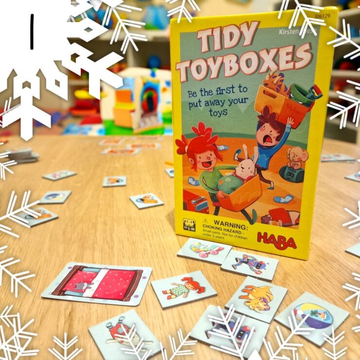 Colorful board game "Tidy Toyboxes" by HABA, featuring playful illustrations on the box and scattered game cards on a wooden table, promoting fun and organization for children.