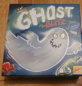 Image of the board game "Ghost Blitz" featuring a playful ghost character on the box cover, designed by Jacques Zeimet and published by Big Potato Games. The box is colorful with illustrations of a mouse, a green bottle, and a red chair, set against a blue background, emphasizing a fun and spooky theme.