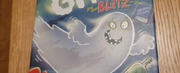Image of the board game "Ghost Blitz" featuring a playful ghost character on the box cover, designed by Jacques Zeimet and published by Big Potato Games. The box is colorful with illustrations of a mouse, a green bottle, and a red chair, set against a blue background, emphasizing a fun and spooky theme.