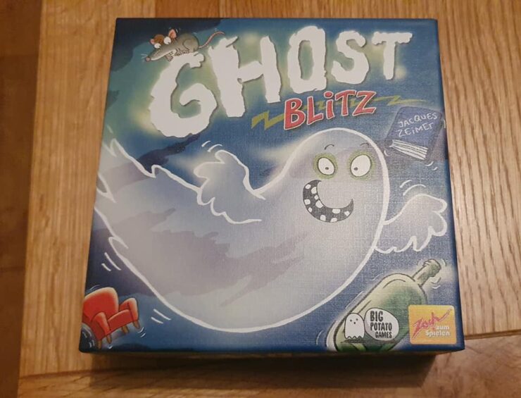 Image of the board game "Ghost Blitz" featuring a playful ghost character on the box cover, designed by Jacques Zeimet and published by Big Potato Games. The box is colorful with illustrations of a mouse, a green bottle, and a red chair, set against a blue background, emphasizing a fun and spooky theme.