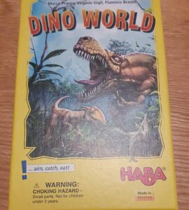 Colorful box of the board game "Dino World" featuring dinosaur illustrations, with a warning label about choking hazards. Designed by Marco Pranzo, Virginio Gigli, and Flaminia Brasini, and manufactured by HABA in Germany.