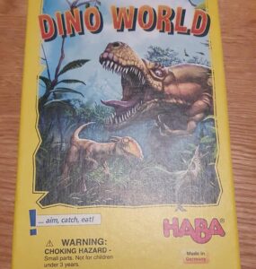Colorful box of the board game "Dino World" featuring dinosaur illustrations, with a warning label about choking hazards. Designed by Marco Pranzo, Virginio Gigli, and Flaminia Brasini, and manufactured by HABA in Germany.