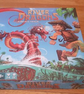 Colorful board game box for "River Dragons" by Roberto Fraga, featuring a boy in a straw hat and a dragon amidst a river scene with tropical plants. Game details indicate it's suitable for ages 8+, for 2-6 players, with a playtime of approximately 25 minutes.