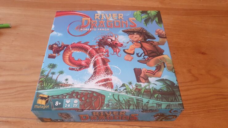 Colorful board game box for "River Dragons" by Roberto Fraga, featuring a boy in a straw hat and a dragon amidst a river scene with tropical plants. Game details indicate it's suitable for ages 8+, for 2-6 players, with a playtime of approximately 25 minutes.