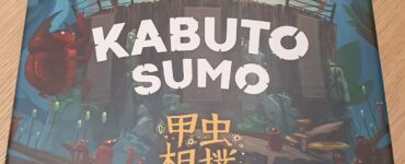 Kabuto Sumo board game box featuring colorful artwork of anthropomorphic insects engaged in a sumo wrestling match, designed by Tony Miller and illustrated by Kwanchai Moriya. The title "Kabuto Sumo" is prominently displayed at the top, with Japanese characters beneath it, set against a whimsical forest background.