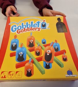 Colorful Gobblet Gobblers game box featuring playful characters and game components, designed for ages 5 and up, suitable for 2 players with a quick 5-minute playtime.