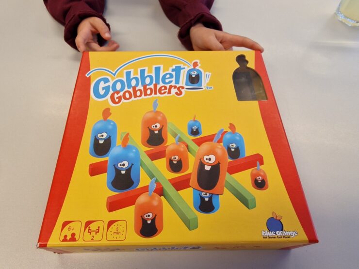 Colorful Gobblet Gobblers game box featuring playful characters and game components, designed for ages 5 and up, suitable for 2 players with a quick 5-minute playtime.