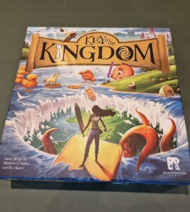 Board game box of "Key to the Kingdom," featuring colorful artwork with a character standing on a yellow path, surrounded by whimsical elements like rubber ducks and an octopus, designed by Matthew O'Malley and Ben Rosset, published by Restoration Games.
