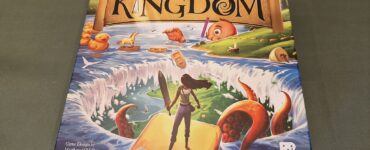Board game box of "Key to the Kingdom," featuring colorful artwork with a character standing on a yellow path, surrounded by whimsical elements like rubber ducks and an octopus, designed by Matthew O'Malley and Ben Rosset, published by Restoration Games.