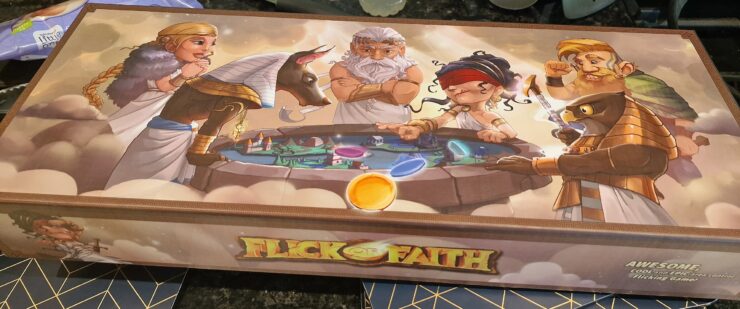 Colorful board game box for "Flick of Faith," featuring mythological characters including gods and a sphinx, with vibrant illustrations and game components displayed.