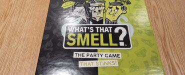 Colorful game box for "What's That Smell?" featuring humorous illustrations and the tagline "The Party Game That Stinks!" Suitable for ages 14 and up, for 2 to 6 players.