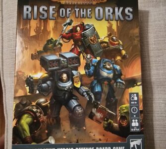 Board game box cover for "Space Marine Adventures: Rise of the Orks," featuring heroic Space Marines battling Orks. The game is designed for 1-5 players, ages 8 and up, and focuses on cooperative defense gameplay.