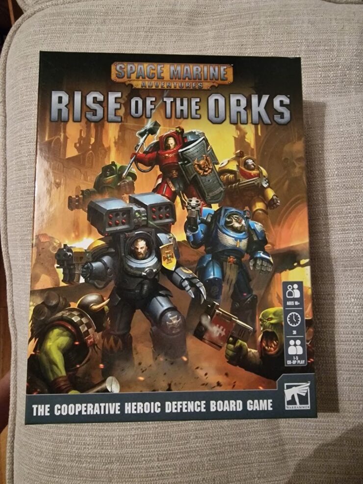 Board game box cover for "Space Marine Adventures: Rise of the Orks," featuring heroic Space Marines battling Orks. The game is designed for 1-5 players, ages 8 and up, and focuses on cooperative defense gameplay.