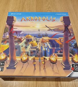 Board game Akropolis box cover featuring a vibrant illustration of an ancient city with pillars, torches, and characters, designed for 2-4 players aged 8 and up, published by Gigamic.