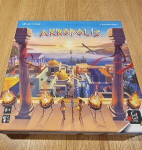 Board game Akropolis box cover featuring a vibrant illustration of an ancient city with pillars, torches, and characters, designed for 2-4 players aged 8 and up, published by Gigamic.