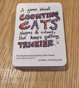Game box for "Counting Cats," designed by Behrooz "Bez" Shariari, featuring colorful text and illustrations. The game focuses on counting cats in various shapes and colors, with increasing difficulty. First edition, printed in 2022.