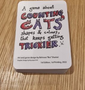 Game box for "Counting Cats," designed by Behrooz "Bez" Shariari, featuring colorful text and illustrations. The game focuses on counting cats in various shapes and colors, with increasing difficulty. First edition, printed in 2022.