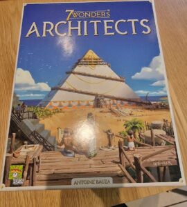 Box cover of the board game "7 Wonders: Architects" by Antoine Bauza, featuring a colorful illustration of a pyramid under construction with characters engaged in architectural activities, set against a beach backdrop. The game is produced by Repos Production.