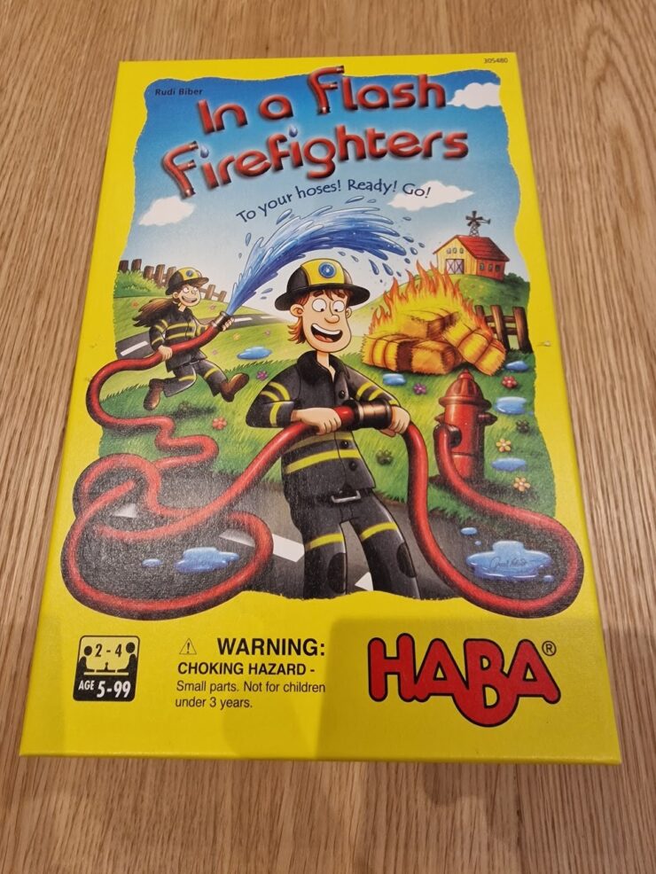 Colorful board game "In a Flash Firefighters" by HABA featuring cartoon firefighters and a fire scene, designed for ages 5 and up. The cover includes a warning about small parts for children under 3 years.