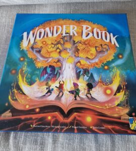 Cover of the board game "Wonder Book," featuring vibrant artwork of a magical tree, characters exploring a fantastical world, and an open book emitting colorful light effects. Ideal for family game nights and fantasy enthusiasts.