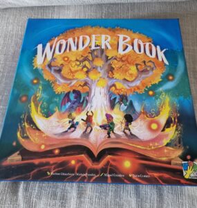 Cover of the board game "Wonder Book," featuring vibrant artwork of a magical tree, characters exploring a fantastical world, and an open book emitting colorful light effects. Ideal for family game nights and fantasy enthusiasts.