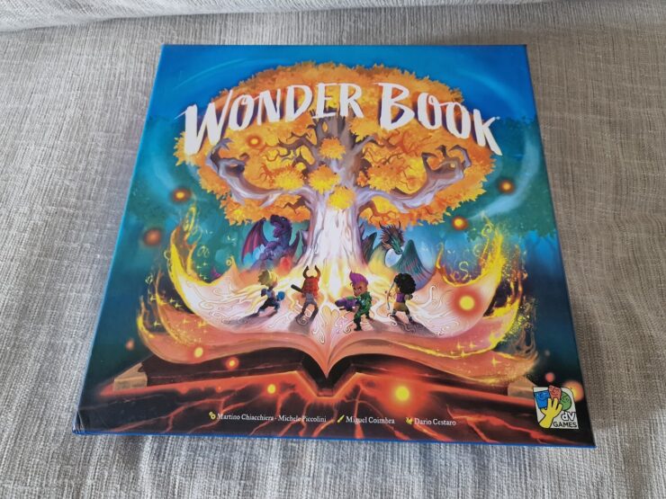 Cover of the board game "Wonder Book," featuring vibrant artwork of a magical tree, characters exploring a fantastical world, and an open book emitting colorful light effects. Ideal for family game nights and fantasy enthusiasts.