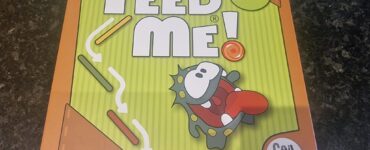Colorful box of the "Feed Me!" puzzle game featuring a cartoon character, labeled for ages 7 and up, with 40 levels of gameplay. Ideal for family fun and cognitive development.