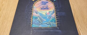 Board game box titled "What Next?" featuring colorful artwork of a pick-your-path adventure with challenges, resting on a wooden surface.