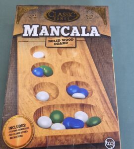 Mancala board game box featuring a solid wood game board, designed for 2 players aged 6 and up, including 48 colored stones and instructions.