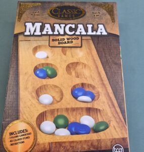 Mancala board game box featuring a solid wood game board, designed for 2 players aged 6 and up, including 48 colored stones and instructions.