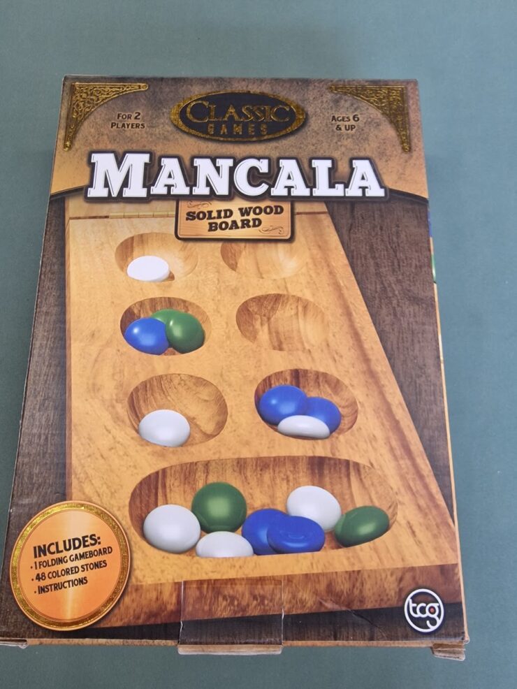 Mancala board game box featuring a solid wood game board, designed for 2 players aged 6 and up, including 48 colored stones and instructions.