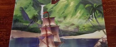 Cover of "The Isle of Cats: Explore & Draw," featuring a colorful illustration of a sailing ship navigating calm waters, surrounded by lush green mountains and tropical palm trees.