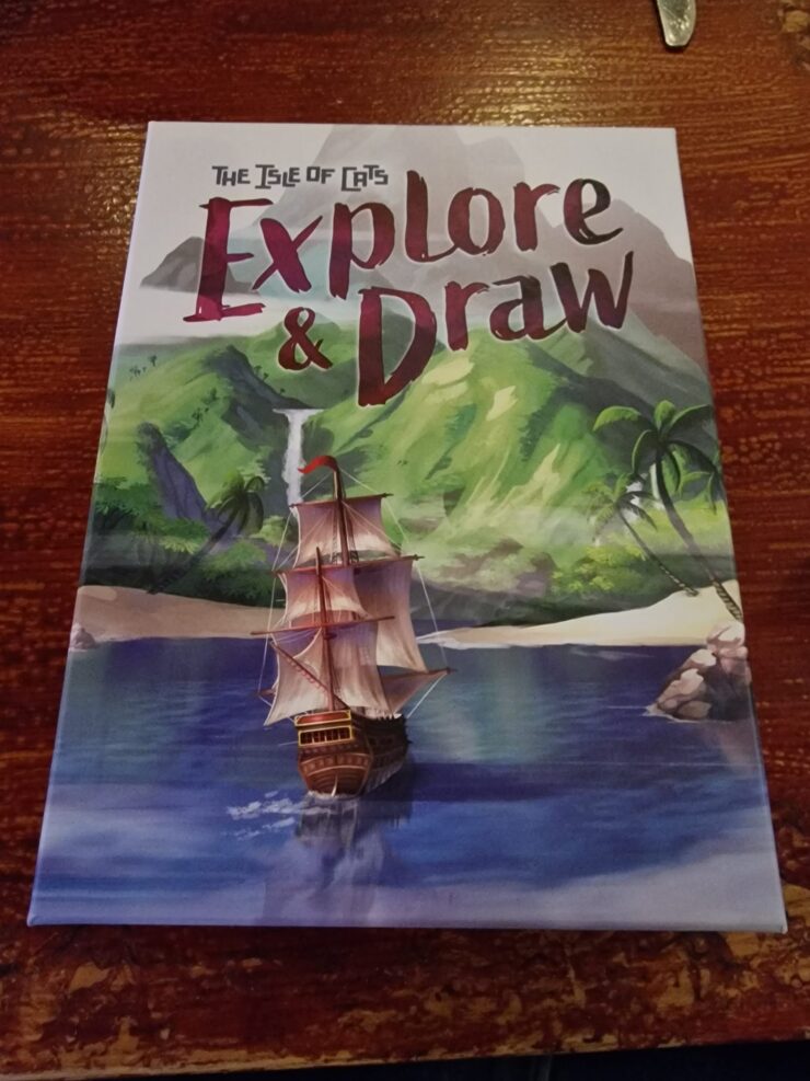 Cover of "The Isle of Cats: Explore & Draw," featuring a colorful illustration of a sailing ship navigating calm waters, surrounded by lush green mountains and tropical palm trees.
