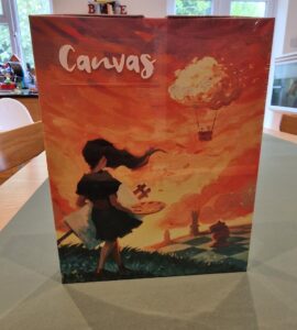 Box cover of the board game "Canvas," featuring a girl holding a paint palette against a vibrant orange sunset with whimsical clouds and a fantasy landscape in the background.