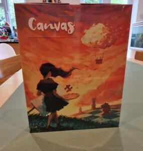 Box cover of the board game "Canvas," featuring a girl holding a paint palette against a vibrant orange sunset with whimsical clouds and a fantasy landscape in the background.