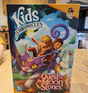 Colorful board game box titled "Kids Chronicles: Quest for the Moon Stones," featuring adventurous characters riding a magical purple cat against a whimsical background. Suitable for ages 7 and up, designed by David Cicurel, published by Lucky Duck Games.