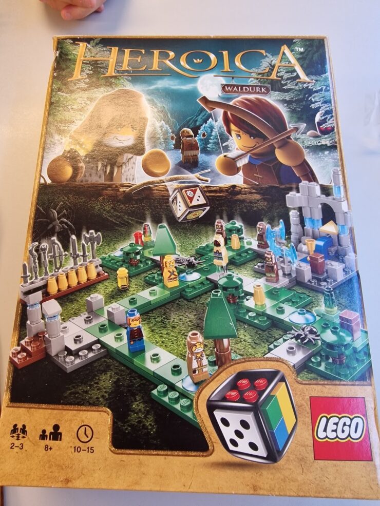 LEGO Heroica Waldurk board game box featuring a colorful game layout with miniature characters, trees, and a dice, designed for 2-3 players aged 8 and up, with an estimated playtime of 10-15 minutes.