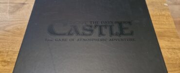 Black game box for "Escape the Dark Castle," featuring the title and tagline "The Game of Atmospheric Adventure" on the lid, placed on a wooden surface.