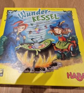 Colorful board game box for "Wunder-Kessel" by HABA, featuring two whimsical witches around a bubbling cauldron, designed for 2 to 4 players aged 5 and up. The vibrant yellow packaging highlights the magical theme and playful illustrations.