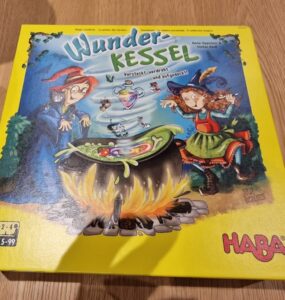 Colorful board game box for "Wunder-Kessel" by HABA, featuring two whimsical witches around a bubbling cauldron, designed for 2 to 4 players aged 5 and up. The vibrant yellow packaging highlights the magical theme and playful illustrations.