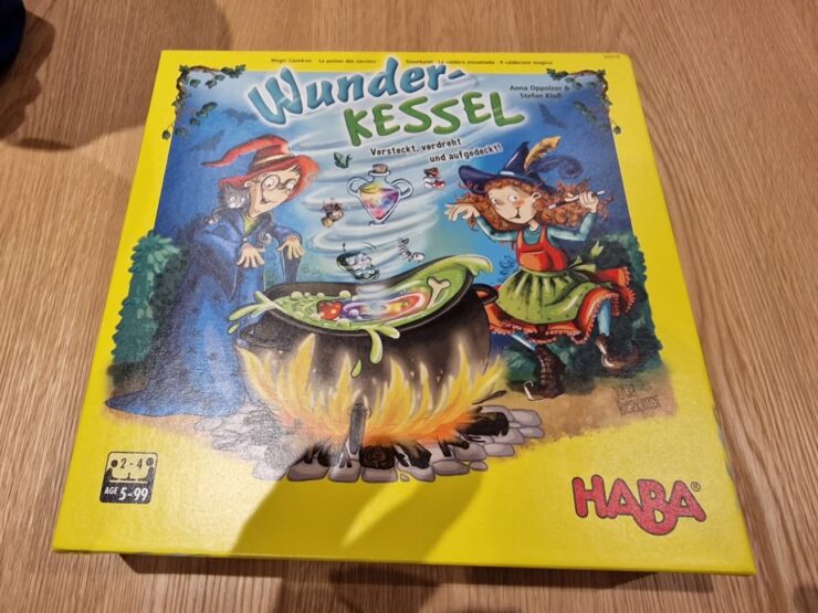 Colorful board game box for "Wunder-Kessel" by HABA, featuring two whimsical witches around a bubbling cauldron, designed for 2 to 4 players aged 5 and up. The vibrant yellow packaging highlights the magical theme and playful illustrations.