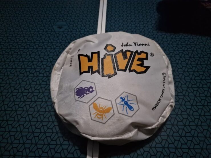 Hive board game packaging featuring the title "HIVE" and illustrations of insect tokens. The design showcases a hexagonal theme, emphasizing the game's strategic gameplay involving bugs like ants and beetles.