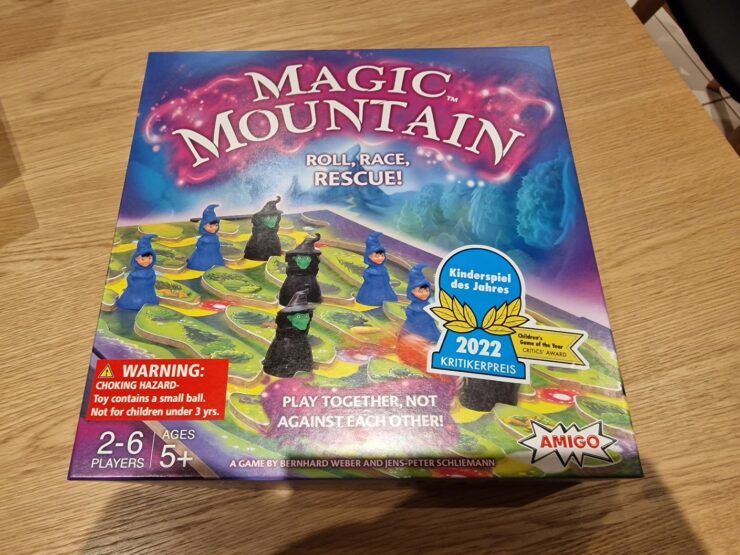 Colorful board game box for "Magic Mountain," featuring playful wizard figures and a vibrant game board. Highlights include "Roll, Race, Rescue!" tagline, age recommendation of 5+, and a warning about small parts. Recognized with the 2022 Children's Game of the Year Critics Award, suitable for 2-6 players.