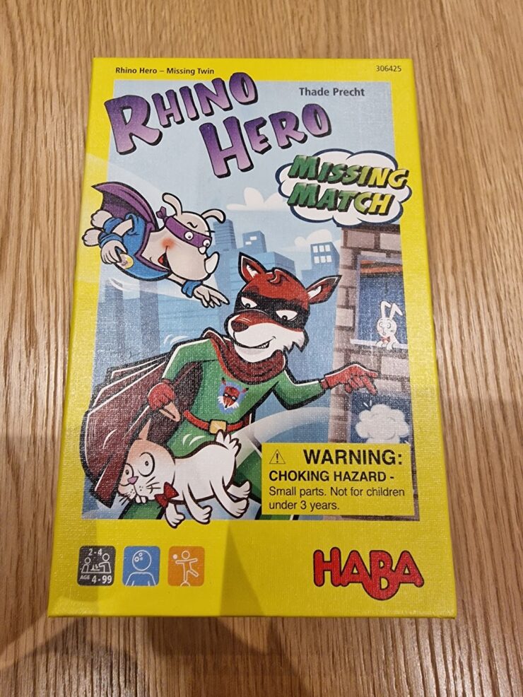 Colorful board game box for "Rhino Hero: Missing Match" by HABA, featuring cartoon characters including a superhero rhino, a cat, and a mouse. The box highlights the game's age recommendation (4-99 years) and includes a choking hazard warning. Ideal for family game nights and children's entertainment.