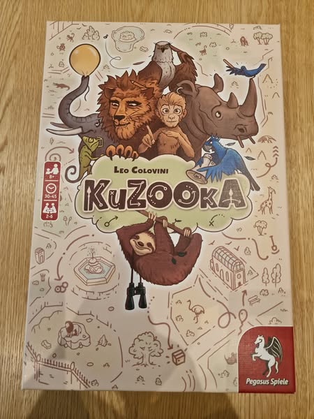 Colorful board game box for "KuZooKa" by Leo Colovini, featuring whimsical animal illustrations including a lion, monkey, sloth, and birds, designed for 2 to 4 players aged 10 and up.
